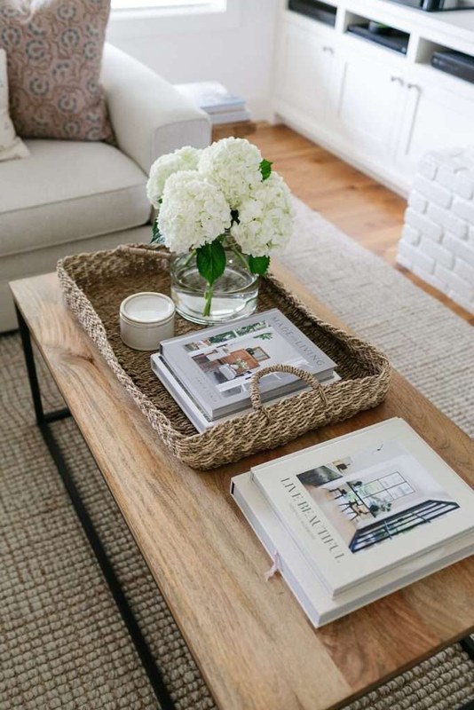 Stack of coffee table books with varied covers arranged on a living room table beside decor objects