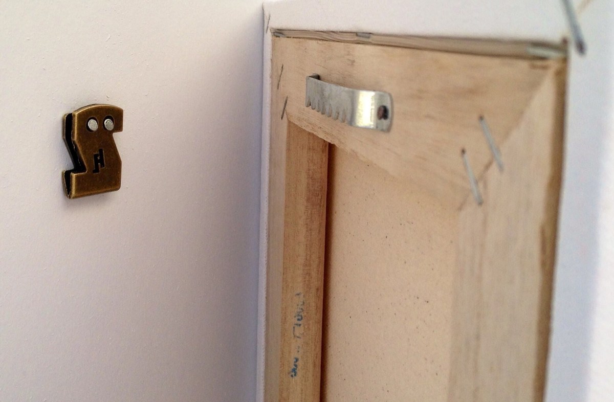 Framed canvas hanging on drywall with a hook and picture wire, positioned above a sofa
