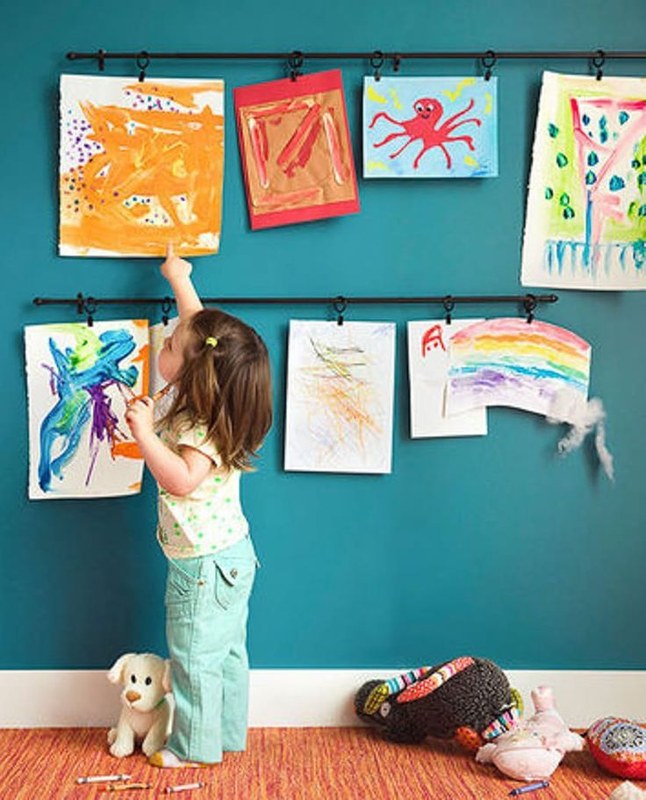 Parent measuring wall space with tape before hanging children’s artwork in a home hallway