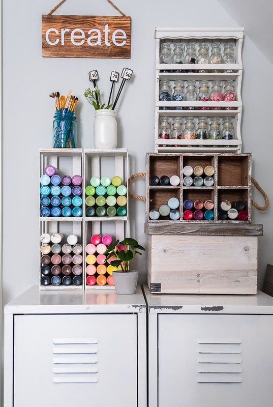 Wall-mounted shelves and drawer bins storing acrylic paint bottles in a compact art room corner