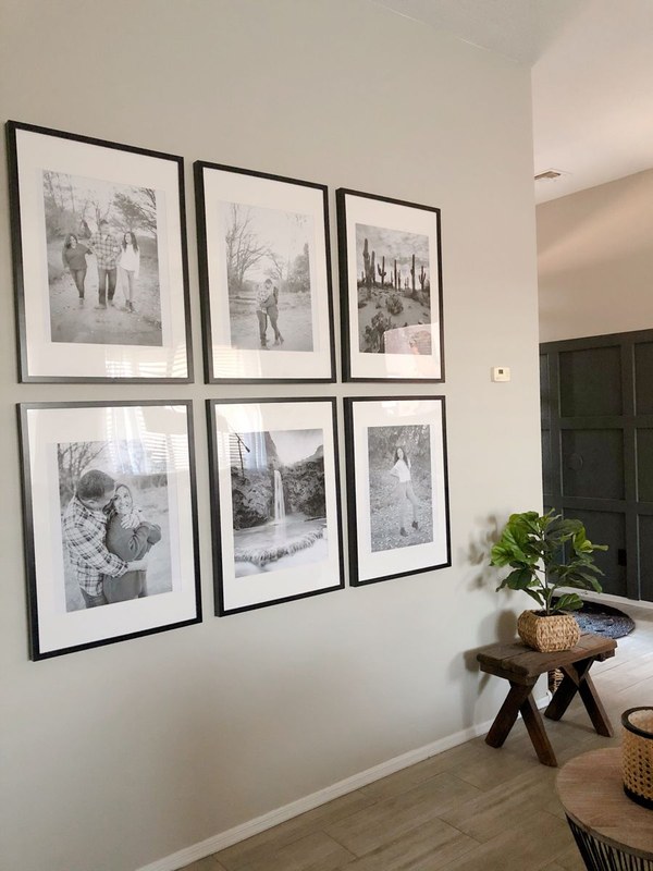 A gallery wall of black and white framed photographs with matching mats and varied frame styles arranged in a grid.