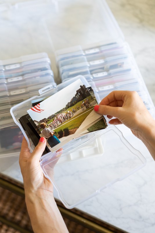 Hands placing old family photographs into an archival storage box on a table